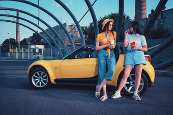 年轻的女士们微笑享受法国薯条纸包饮料纸杯摆姿势黄色的车快食物复制空间