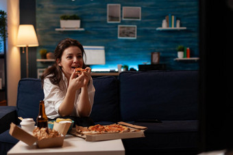 微笑女人吃片热披萨交付坐着沙发上家庭显示电视