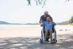 上了年纪的女人坐着轮椅丈夫轮椅用户智能手机采取自拍海滩