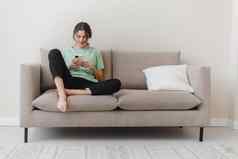 图像快乐乐观年轻的女人坐着在室内首页购物社会媒体移动电话沙发首页