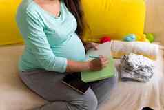 可爱的怀孕了女人写作包装列表孕妇医院笔记本准备袋年轻的莱迪怀孕有趣的花时间沙发首页母亲医学健康护理概念