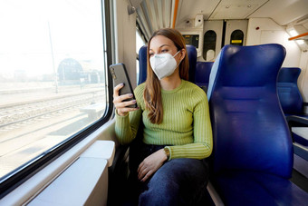 年轻的女人穿医疗面具放松火车座位智能手机应用程序业务女人享受视图发短信移动电话旅行安全生活方式