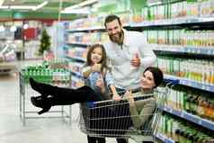 美丽的年轻的父母可爱的女儿微笑选择食物超市父亲推购物车女孩坐