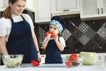 有爱心的妈妈。教学女儿烹饪沙拉厨房年轻的妈妈可爱的可爱的女孩孩子穿围裙切蔬菜刀工作台面站厨房首页