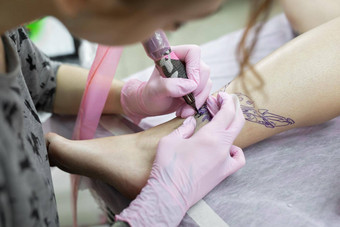 特写镜头纹身艺术家纹身腿年轻的女孩沙龙专业文身的人纹身工作室