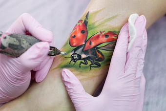 专业纹身艺术家使纹身腿年轻的女孩手纹身艺术家文身的人使纹身特写镜头