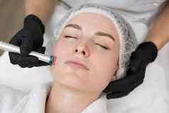 治疗师美容师使激光治疗年轻的女人的脸美水疗中心诊所特写镜头过程激光删除血船只皮肤
