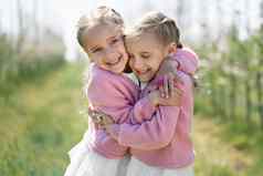 快乐双胞胎姐妹拥抱背景绿色开花苹果果园