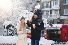 肖像快乐年轻的家庭走冬天城市公园阳光儿子坐着爸爸的脖子