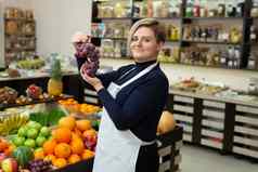 女女售货员帮助客户买水果蔬菜杂货店商店持有手显示葡萄