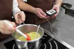 特写镜头手男人。woman-confectioners准备甜点专业厨房烹饪糖浆测量温度