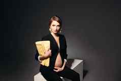 优雅的怀孕了女人坐着黑色的工作室背景