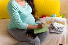 可爱的怀孕了女人写作包装列表孕妇医院笔记本准备袋年轻的莱迪怀孕有趣的花时间沙发首页母亲医学健康护理概念