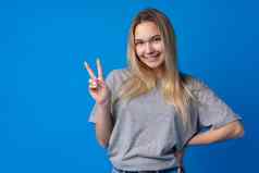 年轻的青少年女孩显示和平象征手指蓝色的背景