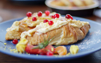 新鲜烤羊角面包白色软甜蜜的奶油红色的浆果板大陆早餐美味的羊角面包奶油黑暗木表格餐厅