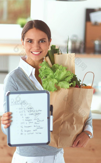年轻的女人持有杂货店购物袋蔬菜站厨房