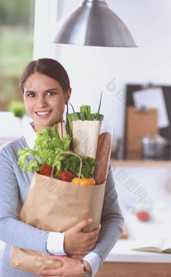年轻的女人持有杂货店购物袋蔬菜站厨房
