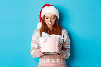 冬天圣诞节夏娃概念感动了受宠若惊红色头发的人女孩盒子圣诞节礼物微笑惊讶站圣诞老人他蓝色的背景