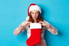 美丽的红色头发的人女孩圣诞老人他开放圣诞节长袜惊讶接收圣诞节礼物站蓝色的背景