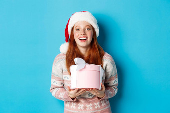 冬天庆祝活动概念快乐红色头发的人女孩接收圣诞节礼物感谢拥抱盒子礼物微笑站圣诞老人他蓝色的背景