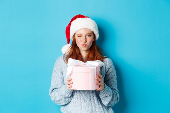 冬天假期圣诞节夏娃概念时髦的红色头发的人女孩毛衣圣诞老人他持有一年礼物相机站蓝色的背景
