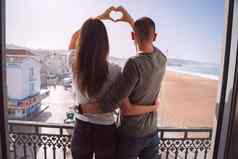年轻的夫妇站阳台使心形状手夫妇爱拥抱支出情人节一天