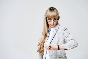 年轻的美丽的金发女郎女人工作室光灰色的背景模型套装眼镜检查时间手表