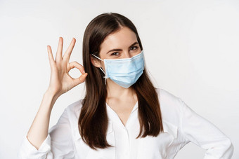关闭肖像微笑女办公室工人医疗面具女人显示标志优秀的标志个人保护科维德流感大流行白色背景