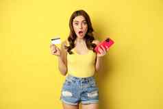 时尚的年轻的浅黑肤色的女人女人持有信贷卡智能手机支付购买订单商店站黄色的背景