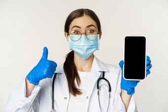 在线医疗概念<strong>热情</strong>的年轻的女人医生脸面具显示拇指移动电话应用程序智能手机屏幕接口白色<strong>背景</strong>