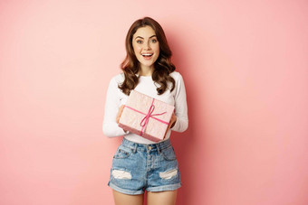 庆祝活动假期快乐美丽的女孩持有礼物包装现在微笑收到惊喜站粉红色的背景