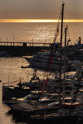 很多巨大的游艇港口摩纳哥日出光滑的董事会电动机船铬镀扶手巨型游艇停泊玛丽娜太阳反射水表面背景