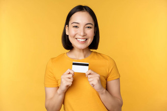 美丽的亚洲女人显示信贷卡微笑推荐银行<strong>服务站</strong>黄色的背景