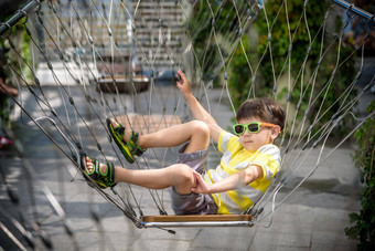可爱的孩子坐着链摇摆不定的夏天假期假期男孩放松快乐穿休闲衣服太阳镜活跃的夏天休闲孩子们城市概念