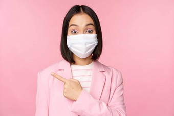 肖像亚洲女商人医疗脸面具西装指出手指左显示<strong>广告公司</strong>横幅工作室粉红色的背景