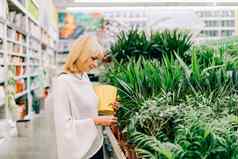 园艺种植购物概念美丽的成熟的成人女人选择室内植物锅温室花园中心高级购买花植物市场商店购物中心