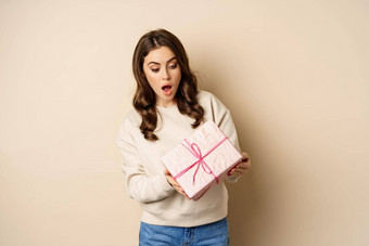 兴奋美丽的女孩粉红色的包装礼物盒子收到礼物站米色背景