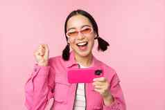 快乐微笑朝鲜文女孩赢得移动电话水平智能手机屏幕欢乐实现目标庆祝站粉红色的背景