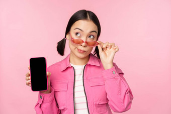 时尚的朝鲜文女孩年轻的女人<strong>太阳镜</strong>显示智能手机屏幕移动电话应用程序接口网站站粉红色的背景