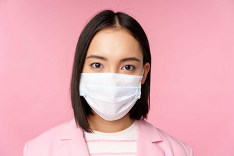 关闭肖像日本女商人医疗脸面具西装相机站粉红色的背景