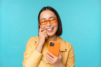快乐时尚的亚洲女孩智能<strong>手机</strong>笑微笑相机站蓝色的背景