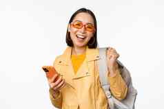 年轻的亚洲女人旅行者女孩旅游太阳镜持有背包移动电话应用程序智能手机站白色背景