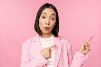热情的专业女商人女售货员指出手指显示广告公司标志摆姿势粉红色的背景