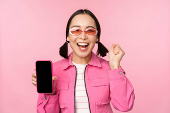 兴奋亚洲女孩笑着说微笑显示移动电话屏幕智能手机应用程序站粉红色的背景