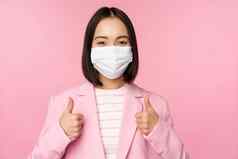 亚洲女商人西装医疗脸面具显示拇指推荐穿个人保护设备办公室科维德流感大流行粉红色的背景