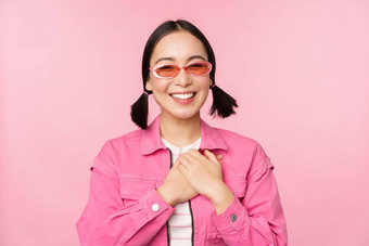 微笑年轻的亚洲女人太阳镜感激持有手心受宠若惊smth站粉红色的背景