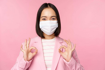 亚洲女商人西装医疗脸面具显示<strong>标志推荐</strong>保护设备办公室科维德流感大流行粉红色的背景