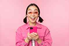 肖像朝鲜文女孩时尚的太阳镜持有移动电话智能手机应用程序站粉红色的背景