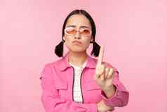 图像时尚的亚洲女孩太阳镜显示停止禁止手势禁忌标志站粉红色的背景