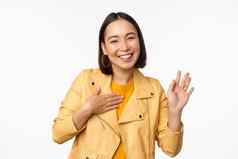 图像友好的亚洲女孩时尚的黄色的外套提高手臂介绍问候挥舞着手站白色背景